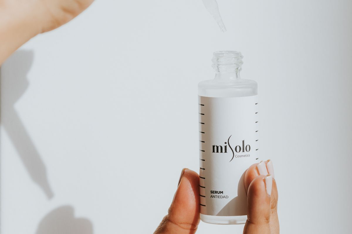 Flacon de sérum cosmétique tenu à la main, pipette au-dessus