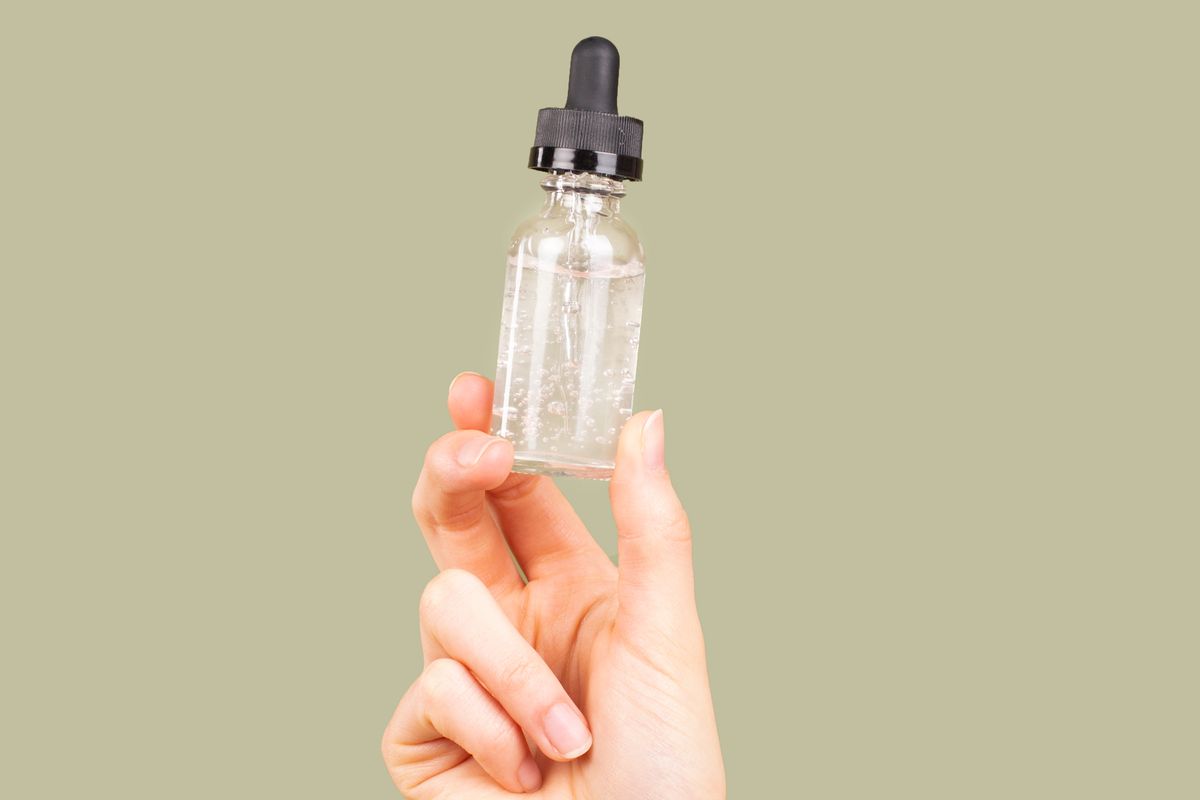 Flacon en verre transparent à pipette tenu entre les doigts