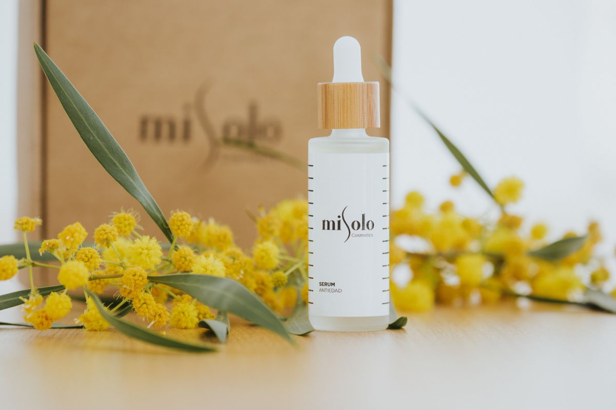 Flacon de sérum cosmétique posé près de fleurs de mimosa